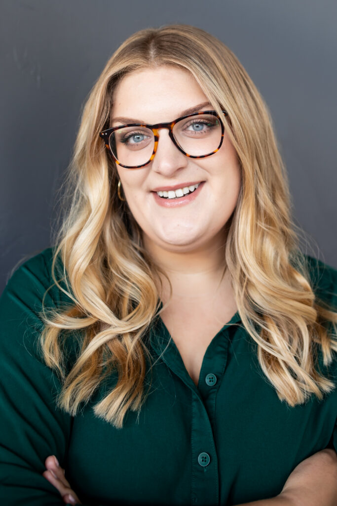 Smiling white woman with blonde hair and glasses in a dark shirt